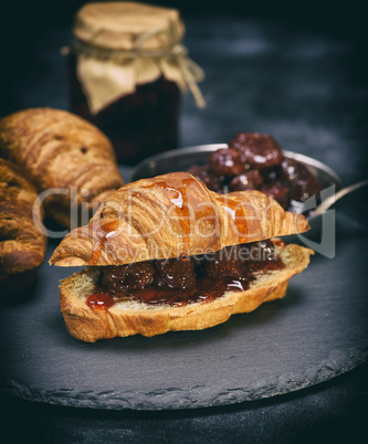 baked croissant with strawberry jam on a black background