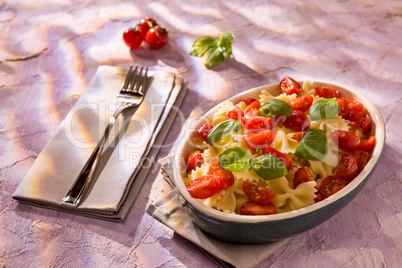 Italian Farfalle pasta with tomatoes and basil over a colored background