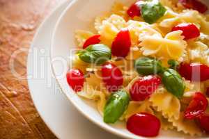 Closeup of Farfalle pasta with cherry tomatoes and basil over a colored background