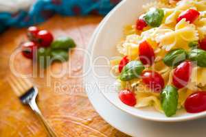 Closeup of Farfalle pasta with cherry tomatoes and basil over a colored background and fork
