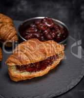 baked croissant with strawberry jam on a black background