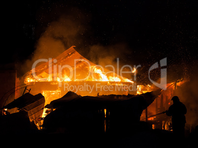 Firefighter at burning fire flame on wooden house roof