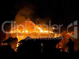 Firefighter at burning fire flame on wooden house roof