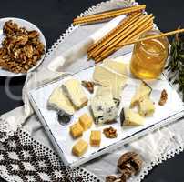 pieces of different cheese on a white wooden board near a jar wi