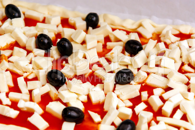 Raw pizza decorated mozzarella, black olives and tomato sauce ready to be baked