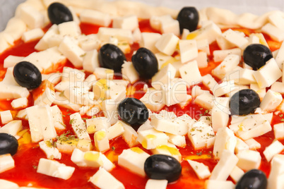 Raw pizza decorated mozzarella, black olives and tomato sauce