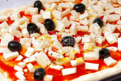 Raw pizza decorated mozzarella, black olives and tomato sauce