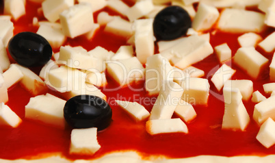 Raw pizza decorated mozzarella, black olives and tomato sauce ready to be baked