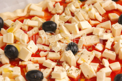 Raw pizza decorated mozzarella, black olives and tomato sauce