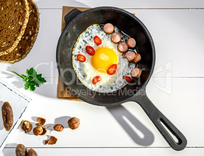 fried chicken egg with pieces of sausage in a black cast-iron fr