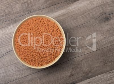 Dry red lentils in a bowl on wooden background.