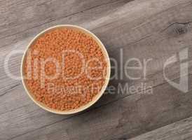 Dry red lentils in a bowl on wooden background.
