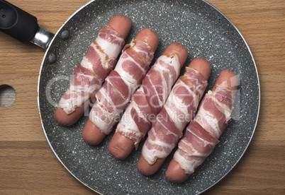 Preparation of raw sausages wrapped spirally in bacon on a fryin
