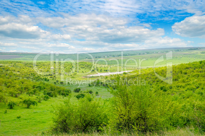 Green field and blue sky. Picturesque hills formed by an old riv