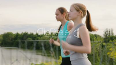 Two Girls Run Along the Walkway at Park Next to a Beautiful Lake