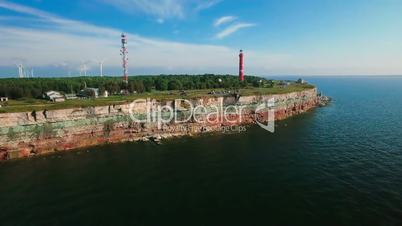 Aerial flying along the coast with a view of the coastline with cliffs from the sea and on land The Old Lighthouse and the wind turbines