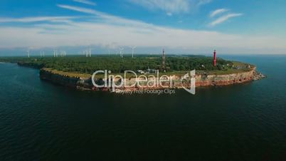 Aerial view of the coastline with rocks from the sea and on the land old lighthouse and wind turbine