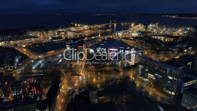 aerial view of the night city with street lighting and moving traffic near the sea and ships in the port