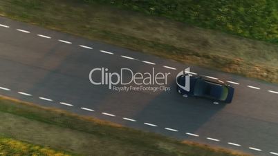 Aerial shot from above driving black car in a field along a rural road in summer at sunset