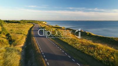 Aerial view of driving black car on the road along the cliff near the sea in summer at sunset. Beautiful cloudy blue sky on the sunset.
