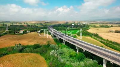 Aerial view of driving vehicles by the highway between fields and rural settlements by summer sunny day in Tuscany, Italy