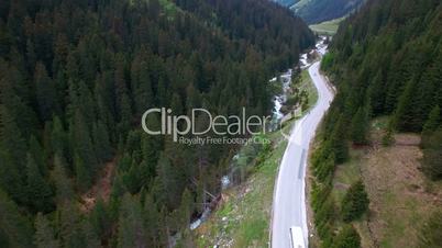 Aerial view of driving white color bus by a road in a mountainous area between the pine forest in Austria