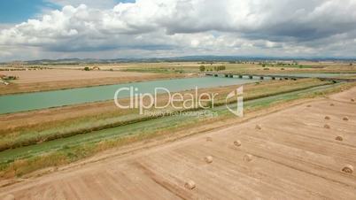 Aerial flight over the field next the river. Aerial view with background of blue sky and clouds. Tuscany, Italy