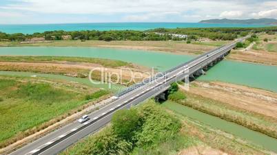 Aerial flight over the green field and a bridge on the river with vehicle on the highway. Tuscany, Italy