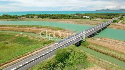 Aerial flight over the green field and a bridge on the river with vehicle on the highway. Tuscany, Italy