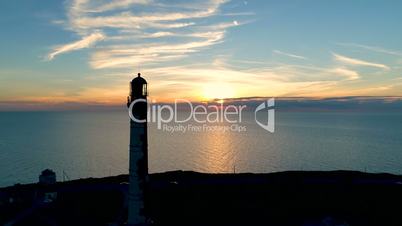 Aerial view of Lighthouse on a sunset background in the sea in summer. Flying of the drone past the lighthouse at sunset