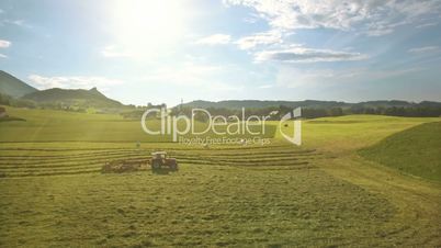 Aerial of Tractor collects Hay on the field in a green line sunny day in the mountains in Austria