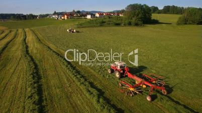 Aerial of Tractor collects Hay on the field in a green line sunny day in the mountains