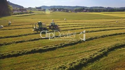 Aerial of tractor makes hay bales and drops them covered in plastic on sunny day in the mountains of Austria
