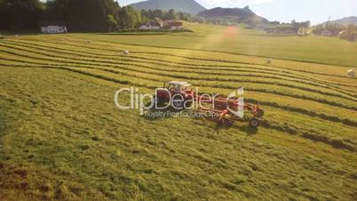 Aerial of Tractor collects Hay on the field in a green line sunny day in the mountains of Austria