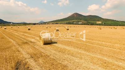 Aerial view of cropped wheat field with bales of hay in the countryside with a beautiful view of the mountain on a sunny day. Czech Republic