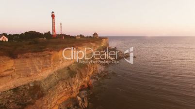 Aerial view of the precipice with terrible rocks by the sea at sunset. Old lighthouse on the edge of the cliff at sunset.