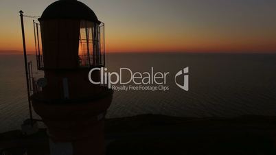 Working old lighthouse on a sunset background in the sea in summer. Aerial flying of the drone past the lighthouse at sunset. Lighthouse gives light signals to ships in the sea