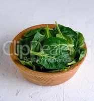 green spinach leaves in a brown wooden bowl on a white surface,