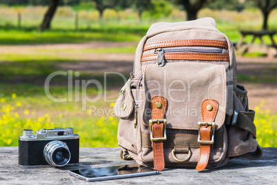 Outfit of traveler,  Different objects on wooden table:  bag, camera, smartphone.