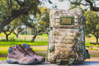 hiking boots and camouflage backpack on a wooden table in nature