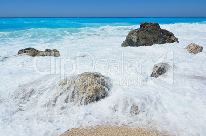 Turqoise water, white sea foam and stones on beach