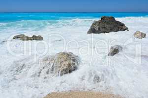 Turqoise water, white sea foam and stones on beach