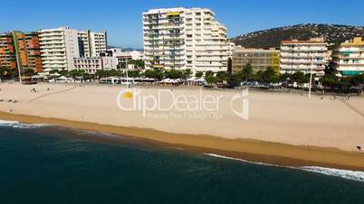 Aerial view of yellow sandy beach with people on the coast in the city on a hot sunny day. Spain, Catalonia