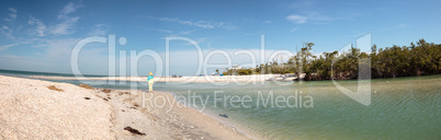 Older woman stands on the white sand beach in front of aqua blue