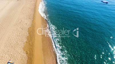 Aerial view of the boat at the yellow sandy beach with people on the coast on a hot sunny day. Spain, Catalonia