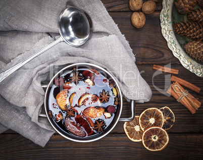 mulled wine with spices and pieces of fruit in a round aluminum