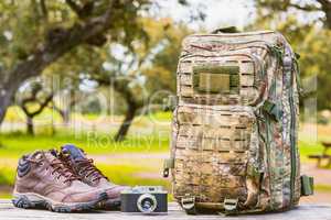 hiking boots, retro camera  and camouflage backpack on a wooden