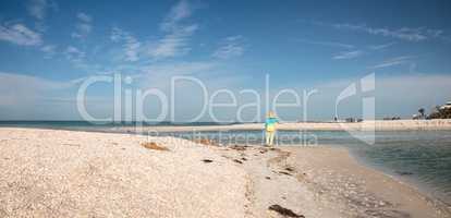 Older woman stands on the white sand beach in front of aqua blue