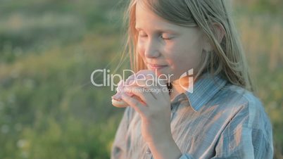 Little girl is eating a sandwich, smiling and looking at the sunset. Close-up.