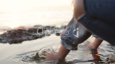 A little girl splashing sea water by the sea coast. Close-up. Sunset at the sea. Slow motion